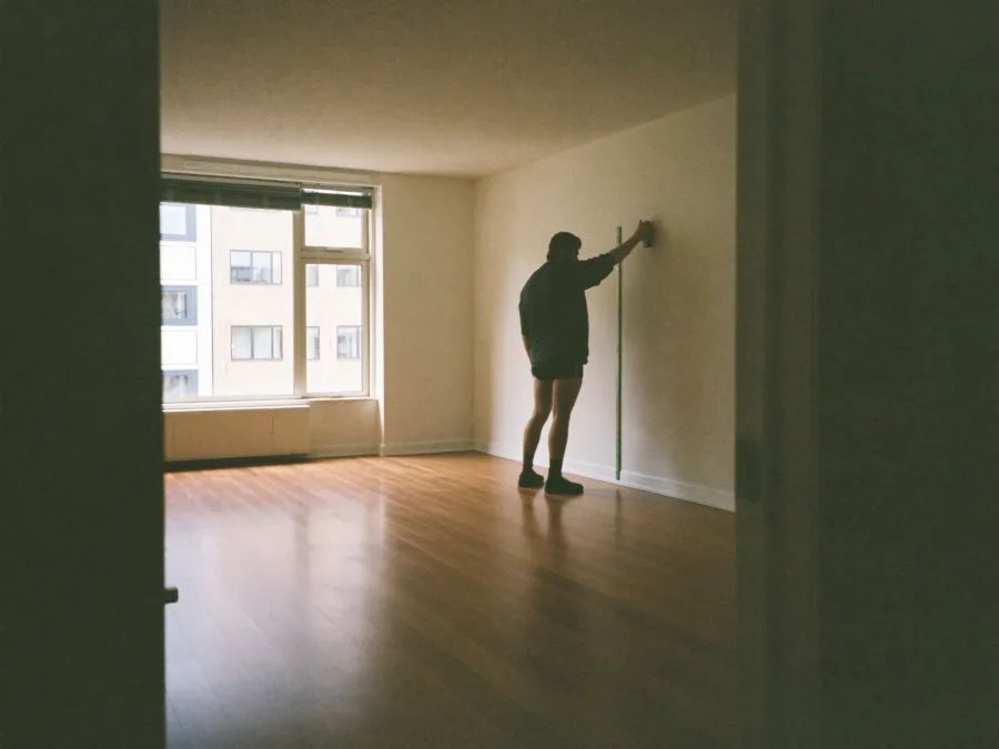Leerer heller Wohnraum mit Parkett, eine Person misst die Wand