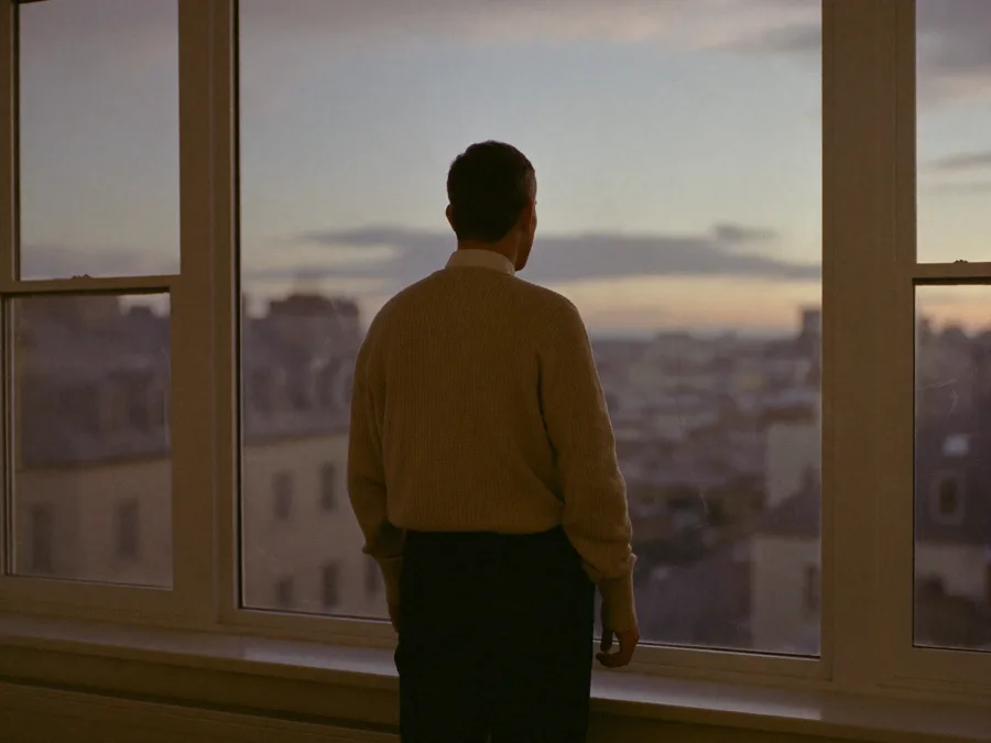 Person am Fenster mit Blick über die Dächer in der Dämmerung